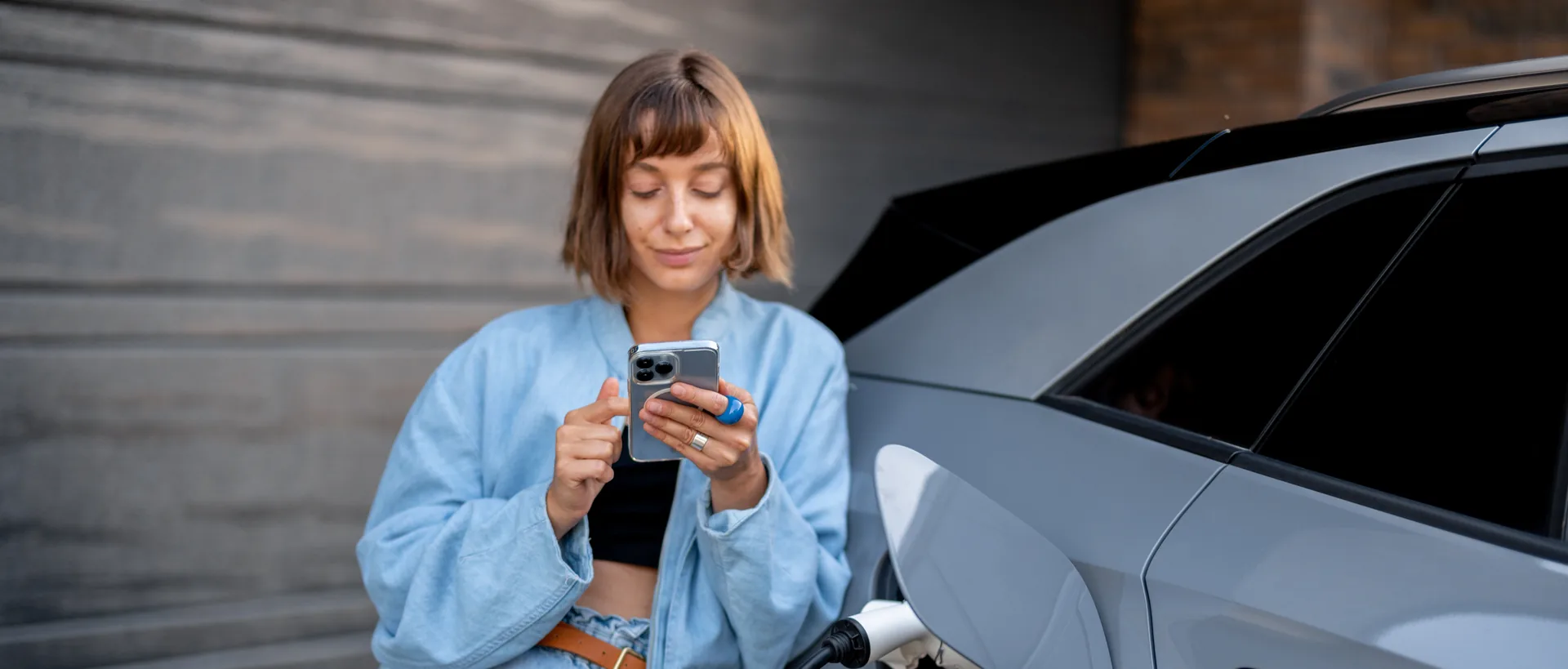 Žena kontroluje v telefóne nabíjanie pripojeného elektromobilu.